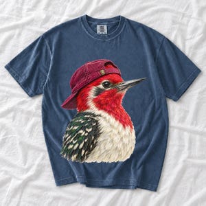 Colored-pencil red-headed woodpecker in side profile wearing a backwards corduroy cap, funny birder t-shirt graphic