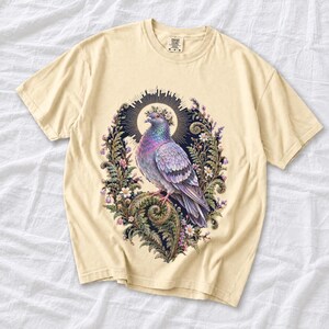 Painted pigeon wearing a daisy crown and glowing halo standing on a fern frond, whimsical cottagecore bird t-shirt art