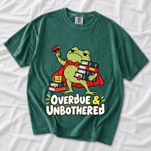 Grumpy cartoon frog librarian holding a stamp and a stack of books with the text Overdue & Unbothered