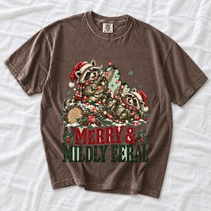 Two raccoons tangled in Christmas lights beside a log with the text Merry & Mildly Feral