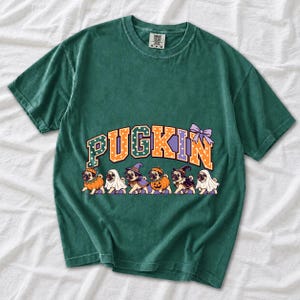 Six pugs in pumpkin, ghost and witch costumes under the arched word PUGKIN, lavender and orange polka-dot varsity style