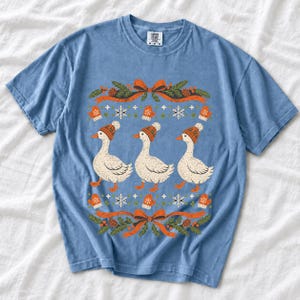 Three geese in pompom knit beanies with mittens, snowflakes and pine borders, retro winter t-shirt graphic
