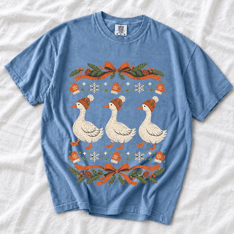 Three geese in pompom knit beanies with mittens, snowflakes and pine borders, retro winter t-shirt graphic
