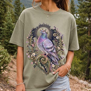 Painted pigeon wearing a daisy crown and glowing halo standing on a fern frond, whimsical cottagecore bird t-shirt art