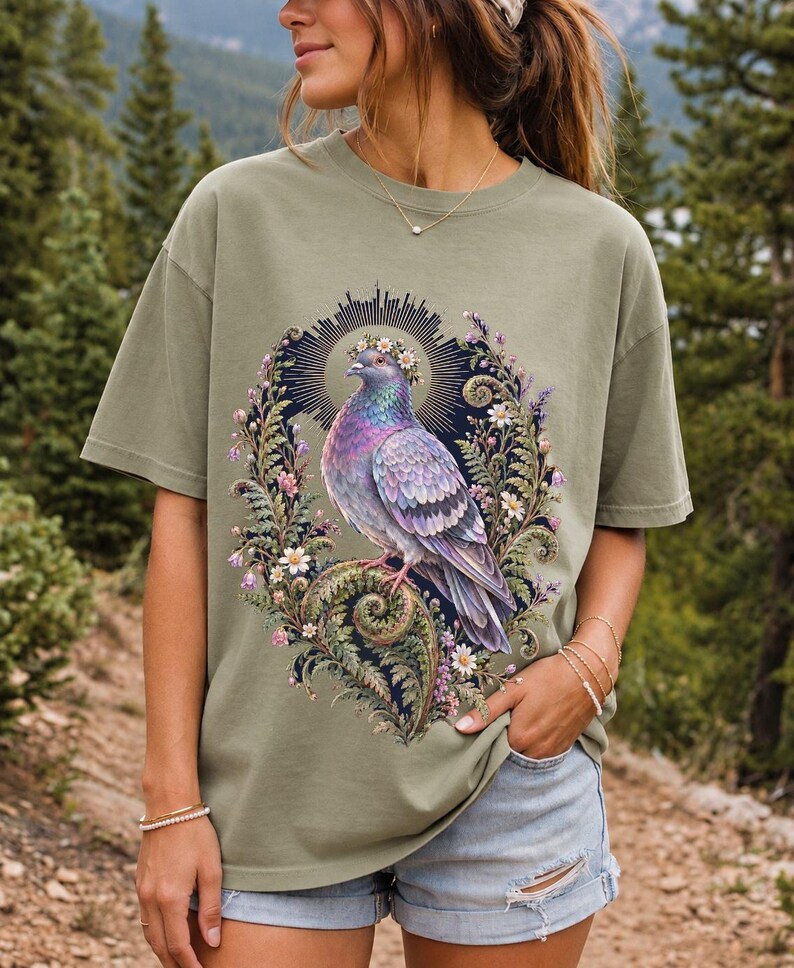 Painted pigeon wearing a daisy crown and glowing halo standing on a fern frond, whimsical cottagecore bird t-shirt art