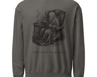 Op de afbeelding: Een antracietgrijze sweater met ronde hals en een zwarte grafische illustratie van een geest die in een fauteuil zit te lezen, met een dampende kop op een bijzettafel. De tekst onder de illustratie luidt in het zwart: "TOO COZY TO HAUNT".