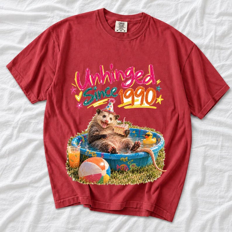 Opossum in party hat in a kiddie pool with cake, 90s film photo style, text "Unhinged Since 1990"