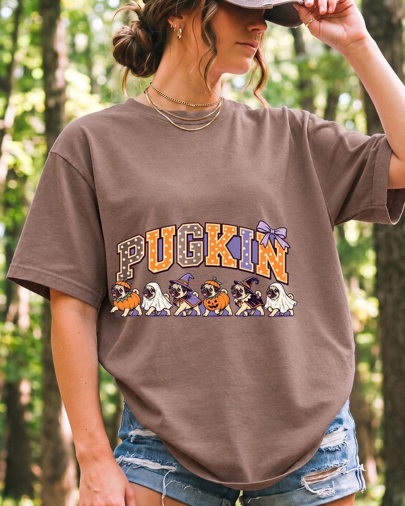 Six pugs in pumpkin, ghost and witch costumes under the arched word PUGKIN, lavender and orange polka-dot varsity style