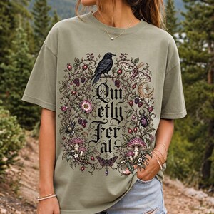 Raven on a wild rose branch with beetles and berries around blackletter text "Quietly Feral"