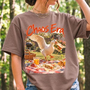 Goose stealing a sandwich from a picnic blanket, 90s film photo style, text "Chaos Era"