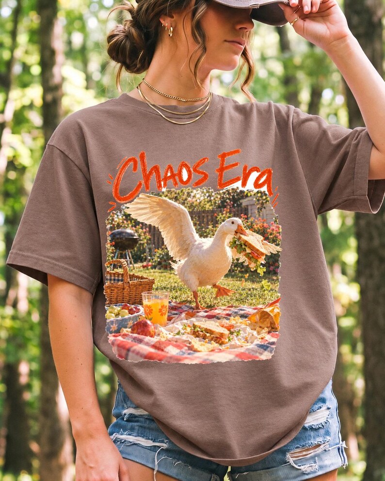 Goose stealing a sandwich from a picnic blanket, 90s film photo style, text "Chaos Era"