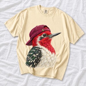Colored-pencil red-headed woodpecker in side profile wearing a backwards corduroy cap, funny birder t-shirt graphic
