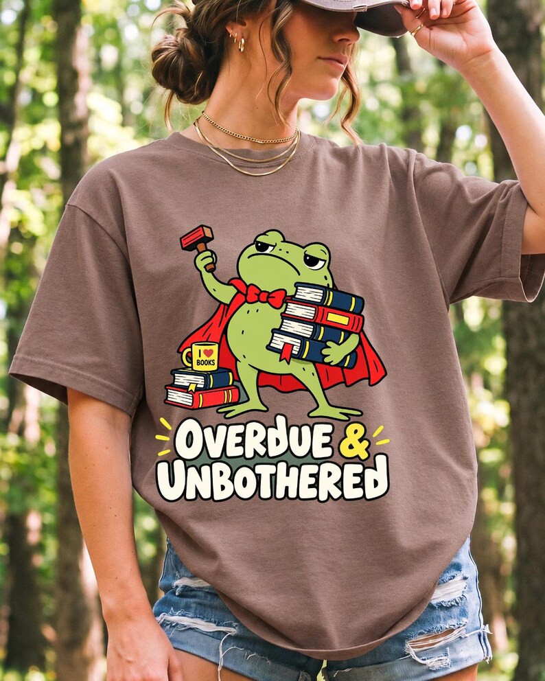 Grumpy cartoon frog librarian holding a stamp and a stack of books with the text Overdue & Unbothered