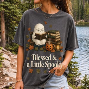 Cute ghost with glasses reading a Bible with a candle and mug, text "Blessed & a Little Spooky", retro fall illustration