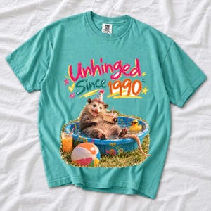 Opossum in party hat in a kiddie pool with cake, 90s film photo style, text "Unhinged Since 1990"