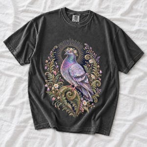 Painted pigeon wearing a daisy crown and glowing halo standing on a fern frond, whimsical cottagecore bird t-shirt art