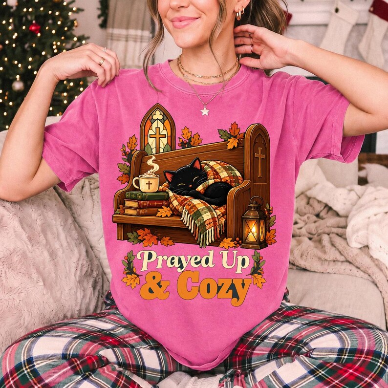 Black cat curled on a church pew with blanket and cocoa among autumn leaves, text "Prayed Up & Cozy", retro illustration