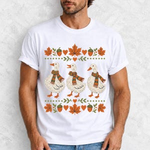Three white ducks in striped scarves with acorn and maple leaf borders, retro screen print fall t-shirt art