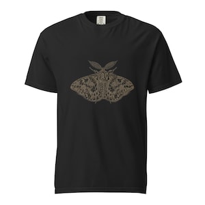 Könnte beinhalten: Ein schwarzes T-Shirt mit kurzen Ärmeln und einer detaillierten, mittigen Grafik eines Nachtfalters in Braun- und Beigetönen. Die Abbildung des Falters zeigt komplexe Flügelmuster und markante Fühler auf dem schwarzen Stoff des T-Shirts.