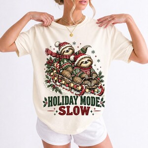 Two sloths in ugly sweaters riding a sled with lights and the text Holiday Mode: Slow
