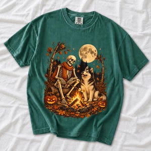 A skeleton in a scarf roasting marshmallows by a campfire beside a husky in an autumn forest under a full moon