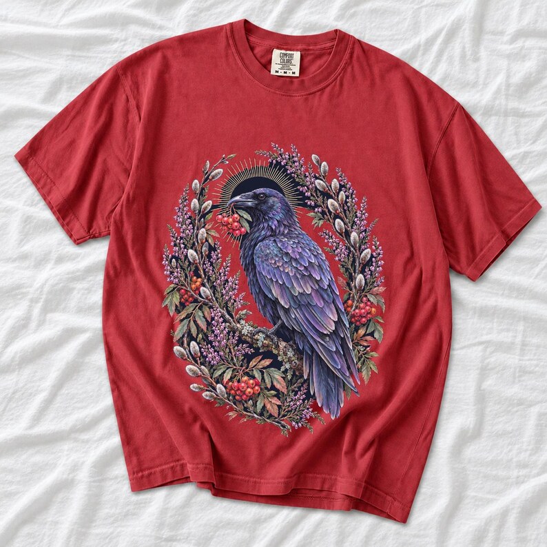 Raven holding a rowan berry inside an oval wreath of heather and catkins, painted cottagecore bird illustration