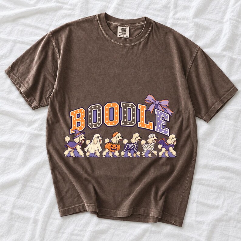 Six poodles in Halloween costumes walking under the arched word BOODLE, lavender and orange polka-dot varsity style