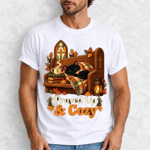 Black cat curled on a church pew with blanket and cocoa among autumn leaves, text "Prayed Up & Cozy", retro illustration