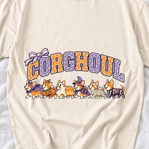 Six corgis in Halloween costumes walking under the arched word CORGHOUL, lavender and orange polka-dot varsity style