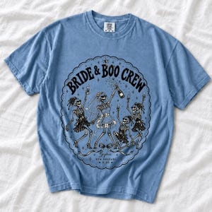 Skeleton bride popping champagne with cheering skeleton bridesmaids and the text Bride & Boo Crew