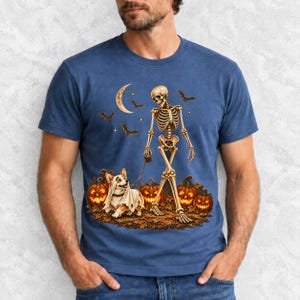A skeleton walking a corgi in a ghost costume past carved pumpkins under a crescent moon