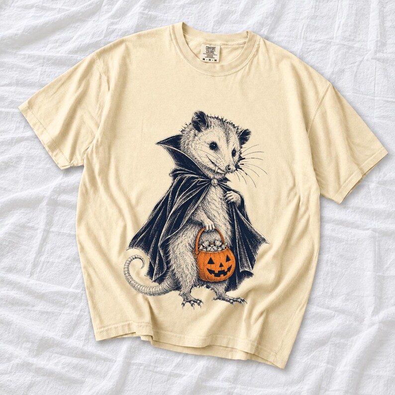 Etched pen illustration of an opossum in a vampire cape holding a candy pumpkin, bone white with orange accent