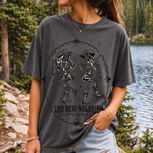 Two cowgirl skeletons in hats line dancing in a starry frame with the text Last Rodeo Nashville
