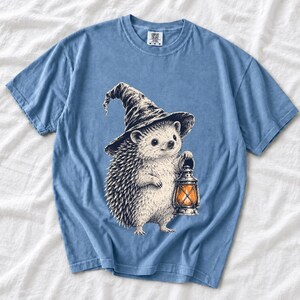 Etched pen illustration of a hedgehog in a witch hat holding a lantern, bone white with orange accent