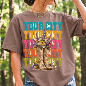 Tan cowboy boots with lavender and wildflowers over a five-line stacked personalized city word in retro colors
