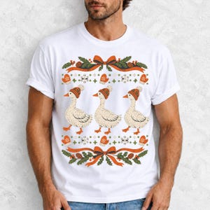 Three geese in pompom knit beanies with mittens, snowflakes and pine borders, retro winter t-shirt graphic