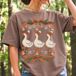 Three geese in pompom knit beanies with mittens, snowflakes and pine borders, retro winter t-shirt graphic