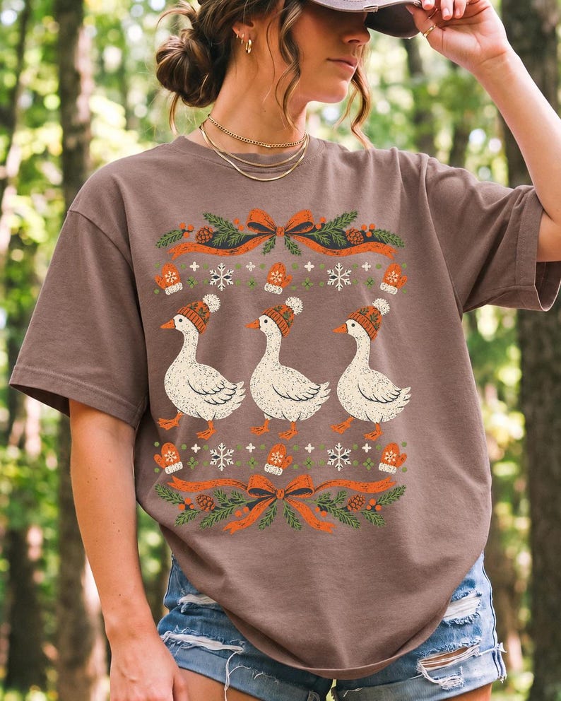Three geese in pompom knit beanies with mittens, snowflakes and pine borders, retro winter t-shirt graphic