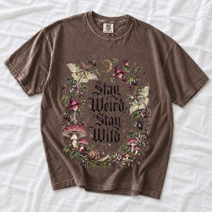 Victorian-style wreath of nightshade, luna moths and toadstools around the words "Stay Weird, Stay Wild"