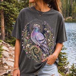Painted pigeon wearing a daisy crown and glowing halo standing on a fern frond, whimsical cottagecore bird t-shirt art