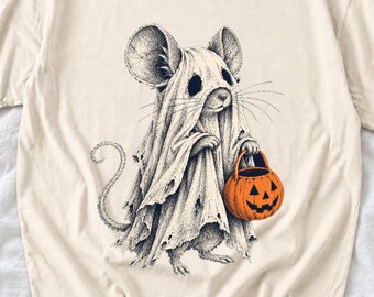 May include: A cream-colored t-shirt featuring a black and white ink-style illustration of a mouse wearing a tattered ghost costume. The mouse is holding a bright orange jack-o'-lantern candy bucket with a carved face.