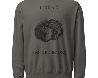 Op de afbeelding: Een antracietgrijze sweater met ronde hals en een afbeelding van een boek dat is omwikkeld met kettingen en een hangslot. De tekst "I READ" staat boven de illustratie van het boek en "BANNED BOOKS" staat eronder in het zwart gedrukt.