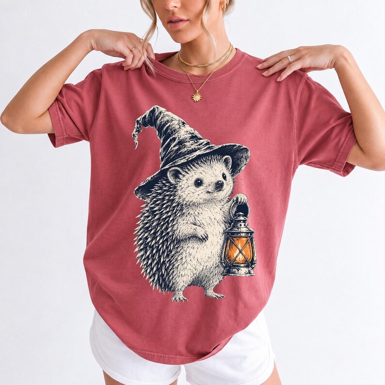 Etched pen illustration of a hedgehog in a witch hat holding a lantern, bone white with orange accent