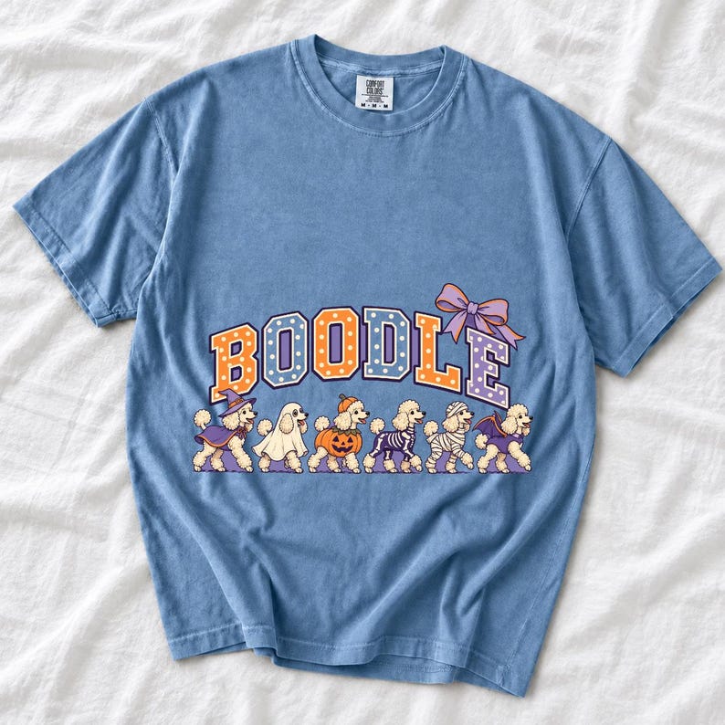 Six poodles in Halloween costumes walking under the arched word BOODLE, lavender and orange polka-dot varsity style