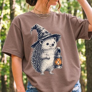 Etched pen illustration of a hedgehog in a witch hat holding a lantern, bone white with orange accent