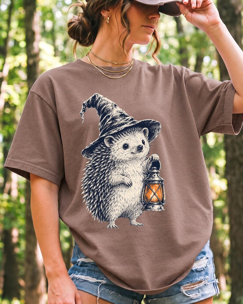 Etched pen illustration of a hedgehog in a witch hat holding a lantern, bone white with orange accent