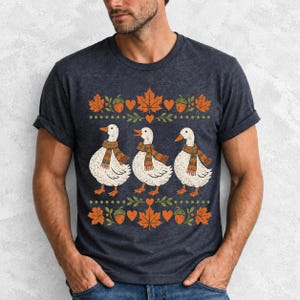 Three white ducks in striped scarves with acorn and maple leaf borders, retro screen print fall t-shirt art