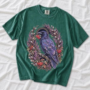 Raven holding a rowan berry inside an oval wreath of heather and catkins, painted cottagecore bird illustration