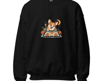 May include: A black long-sleeve sweatshirt featuring a central graphic of a cartoon corgi wearing an oven mitt, baking pumpkin and star-shaped cookies on a tray, surrounded by pumpkins, a crescent moon, and small bats in a dark setting.