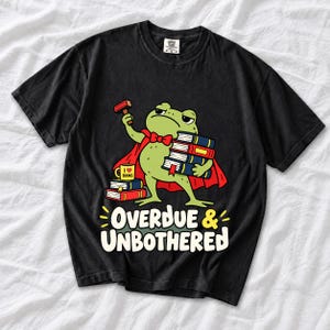 Grumpy cartoon frog librarian holding a stamp and a stack of books with the text Overdue & Unbothered